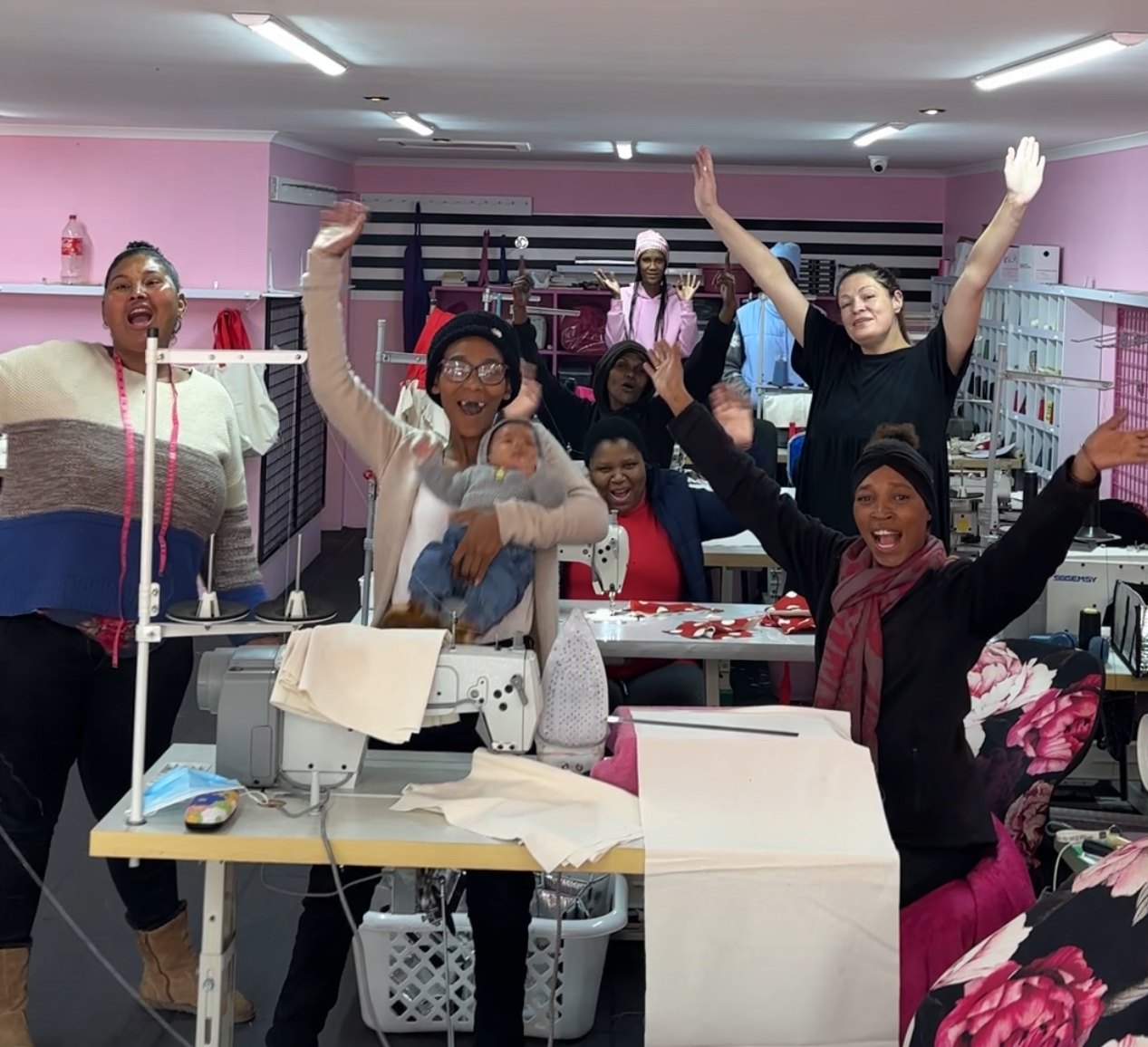 The Wild Mongoo women cheering together with hands in the air in their pink George sewing workshop